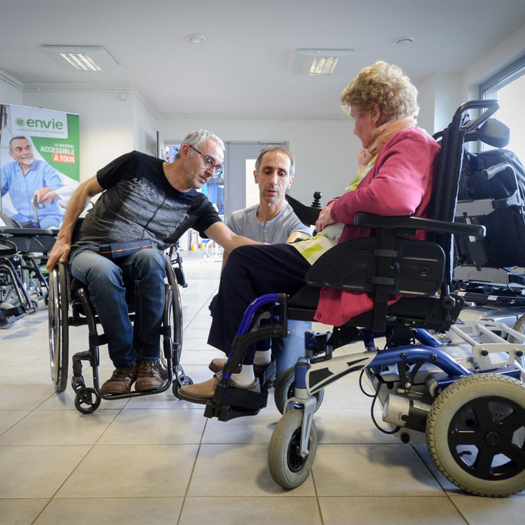 Deux clients essaient des fauteuils roulants en compagnie d'un conseiller vente dans le magasin Envie Autonomie proposant du matériel médical d'occasion